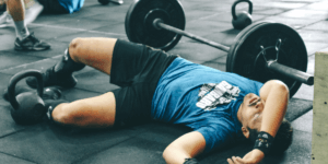 athlete lying on floor next to barbell after a crossfit open workout